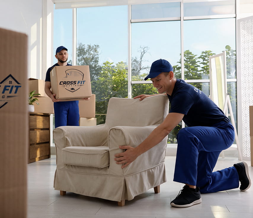 Cross Fit Moving crew positioning an armchair and carrying a box inside a bright home